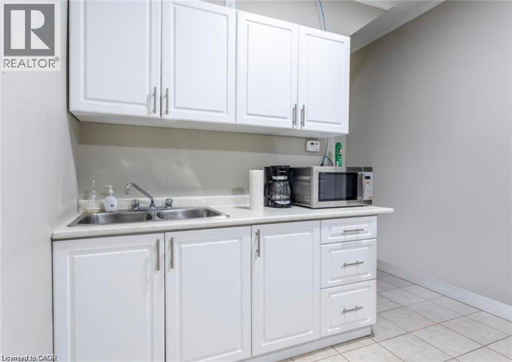 Kitchenette with white cabinetry, a double stainless steel sink, and light-colored countertops - 833 King Street E, Hamilton, ON