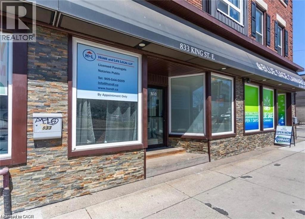 The property features a stone facade and large front windows, with an awning extending across the storefront - 833 King Street E, Hamilton, ON