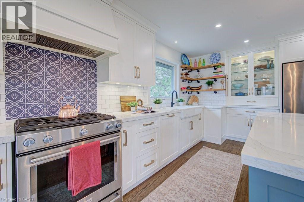 Kitchen featuring a stainless steel range with a decorative tile backsplash, complemented by white cabinetry with gold hardware - 1486 Augustine Drive, Burlington, ON - Indoor Photo Showing Kitchen