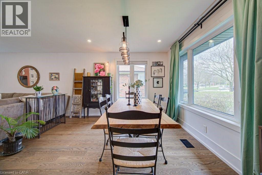 Open-concept dining area featuring wood-finish flooring, a linear pendant light fixture, and a large window with white trim - 1486 Augustine Drive, Burlington, ON - Indoor Photo Showing Dining Room