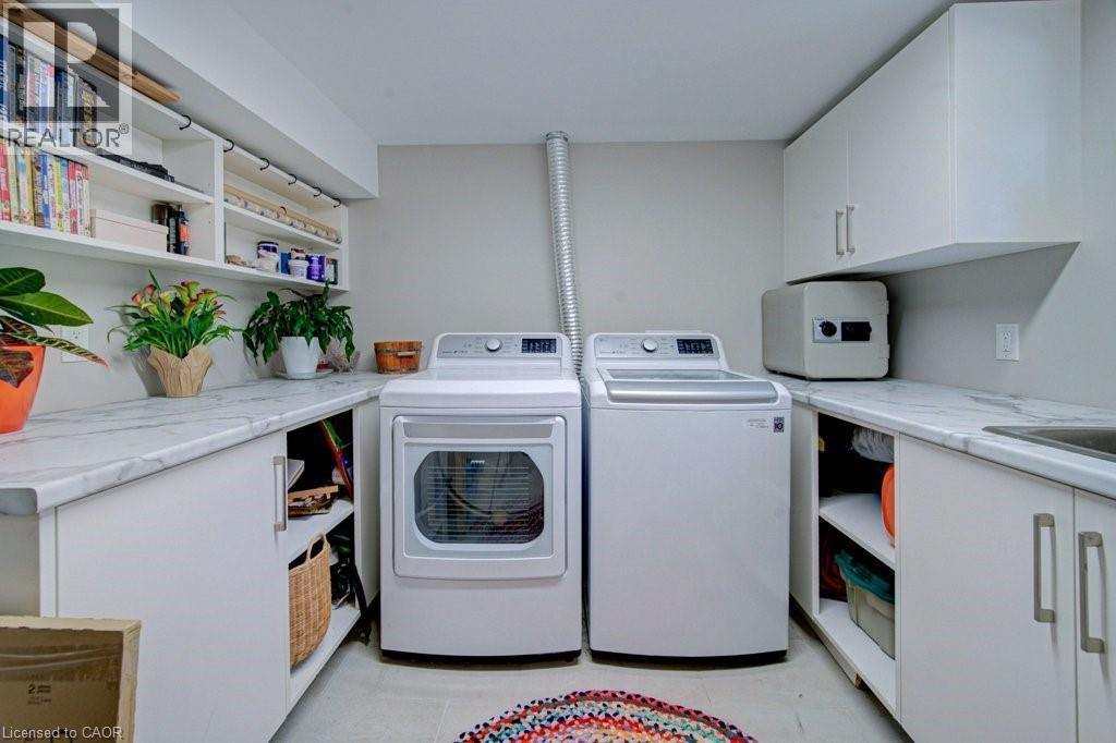 Dedicated utility space featuring a washer and dryer, extensive countertop space with a marble-finish surface, white cabinetry, open shelving, and an integrated sink basin - 1486 Augustine Drive, Burlington, ON - Indoor Photo Showing Laundry Room