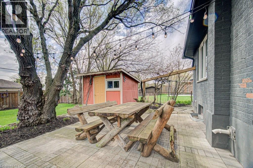 Expansive paver patio featuring a mature tree, string lighting, and a red storage shed with a yellow door - 1486 Augustine Drive, Burlington, ON - Outdoor