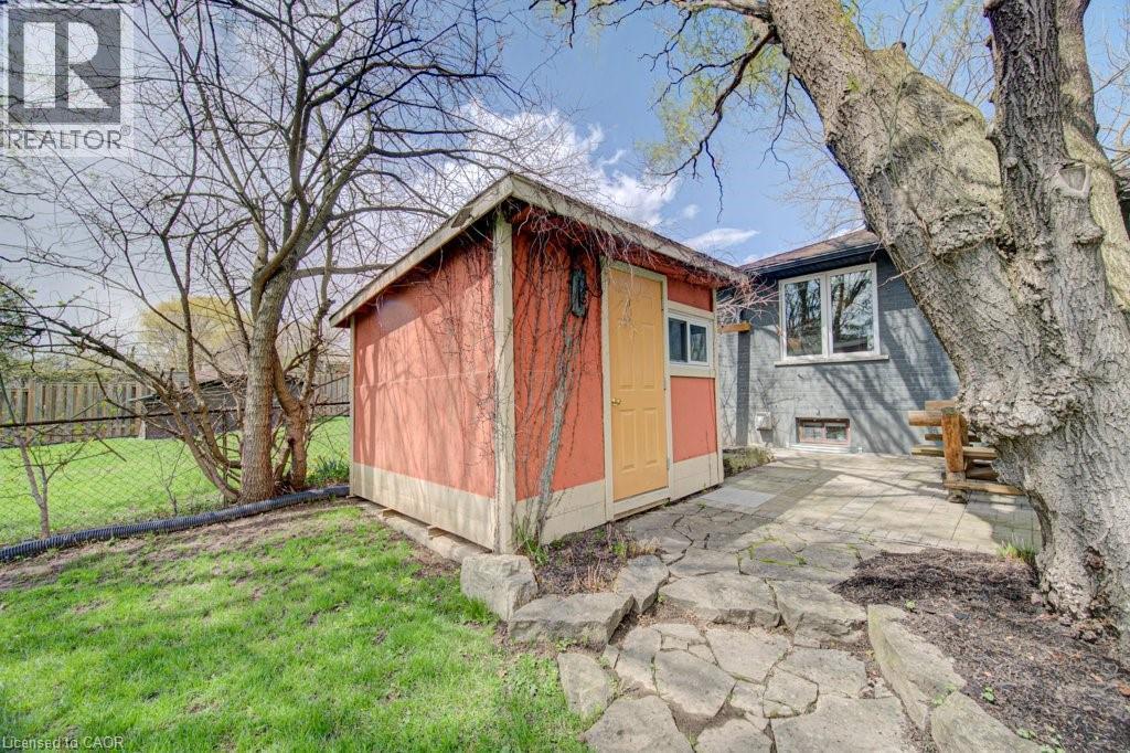 Exterior storage shed with a contrasting yellow door, stone pathway, and mature tree landscaping - 1486 Augustine Drive, Burlington, ON - Outdoor