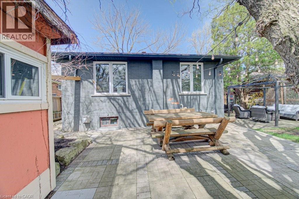 Paved patio with a wooden picnic table, bordered by a dark gray brick exterior and garden beds - 1486 Augustine Drive, Burlington, ON - Outdoor