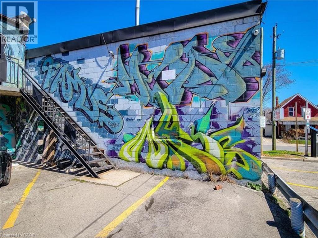 Exterior block wall featuring colorful graphic art and a black metal exterior staircase - 310 Barton Street E Unit# A, Hamilton, ON - Outdoor
