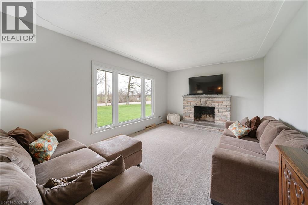 Living area featuring a stone-clad fireplace with hearth, a wall-mounted flat-screen television, and expansive windows - 2223 Hall Road, Binbrook, ON - Indoor Photo Showing Living Room With Fireplace
