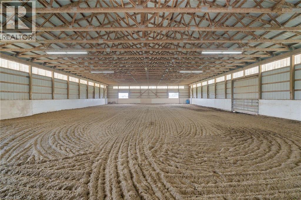 Spacious indoor arena featuring a prepared sand footing, exposed wood beam ceiling, ample overhead lighting, and perimeter translucent panels for natural illumination - 2223 Hall Road, Binbrook, ON - Indoor