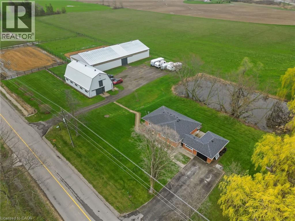 Expansive property featuring a single-story brick residence with dark shingle roofing, multiple outbuildings, a visible pond, and a fenced riding arena - 2223 Hall Road, Binbrook, ON - Outdoor With View