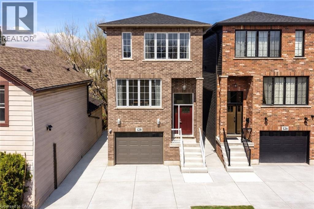 Brick facade home featuring a red entry door, white window frames, a single-car garage, and a paved driveway - 128 Canada Street, Hamilton, ON - Outdoor With Facade