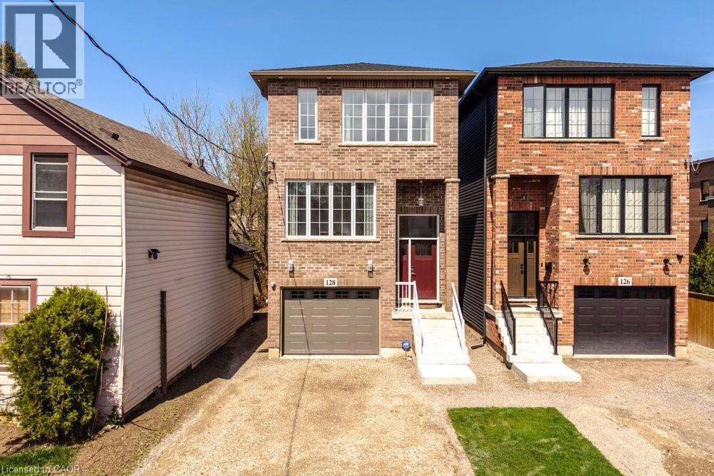 Brick facade home featuring a single garage, a red front door, white trimmed windows, and a paved driveway - 128 Canada Street, Hamilton, ON - Outdoor