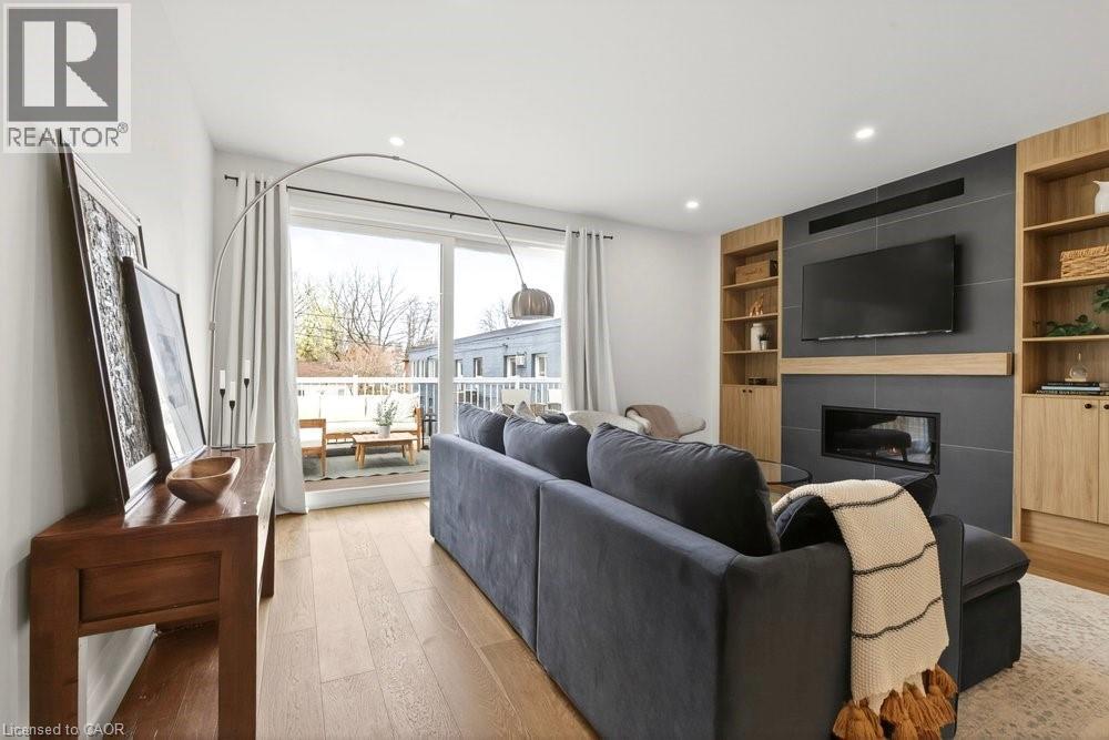 Living area featuring wood-finish flooring, a contemporary fireplace with dark tile surround, built-in shelving, recessed lighting, and sliding glass doors opening to a balcony - 128 Canada Street, Hamilton, ON - Indoor Photo Showing Living Room With Fireplace