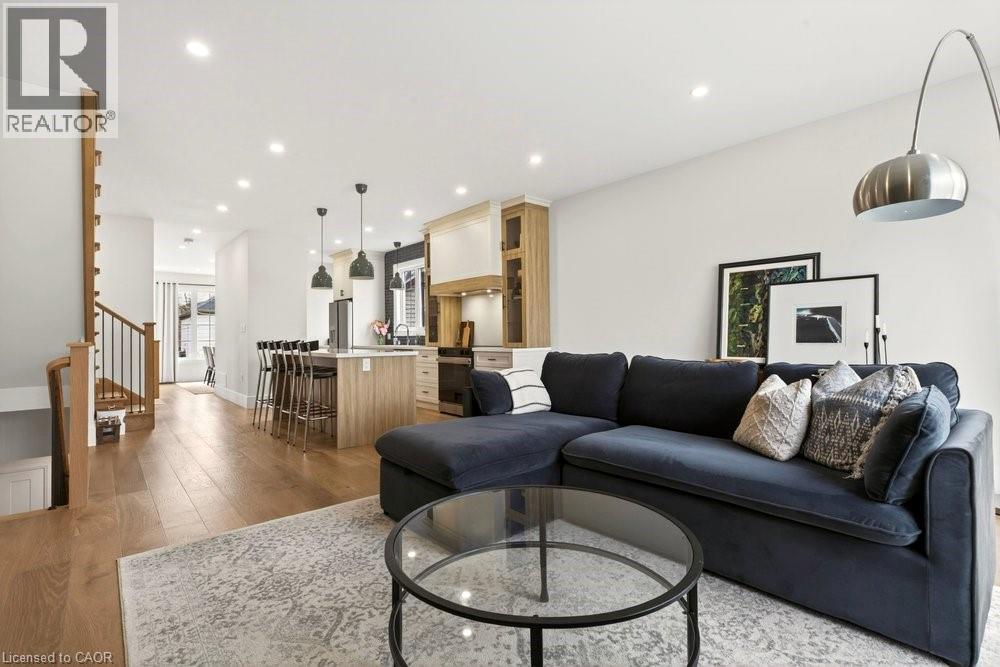 Open-concept living space featuring wood-finish flooring, recessed lighting, a kitchen island with seating, and a staircase with metal balusters - 128 Canada Street, Hamilton, ON - Indoor Photo Showing Living Room