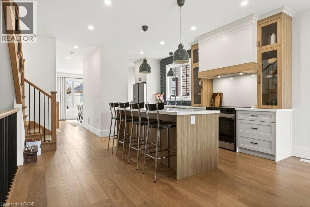 Open-concept kitchen with wood-finish flooring, a central island featuring bar seating, pendant lighting, and stainless steel appliances - 128 Canada Street, Hamilton, ON - Indoor Photo Showing Kitchen With Upgraded Kitchen