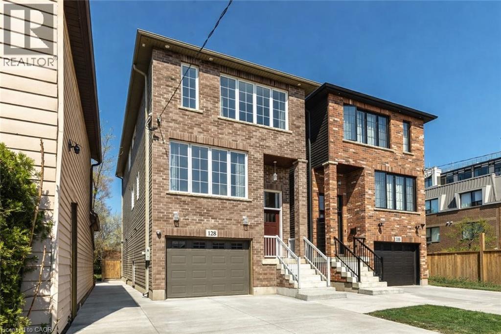 Brick facade townhouse featuring white-framed windows, an attached garage, and a concrete driveway - 128 Canada Street, Hamilton, ON - Outdoor With Facade