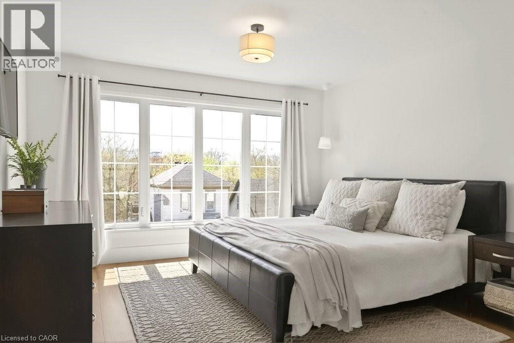 Hardwood flooring with a large window array, white walls, and a ceiling-mounted light fixture - 128 Canada Street, Hamilton, ON - Indoor Photo Showing Bedroom
