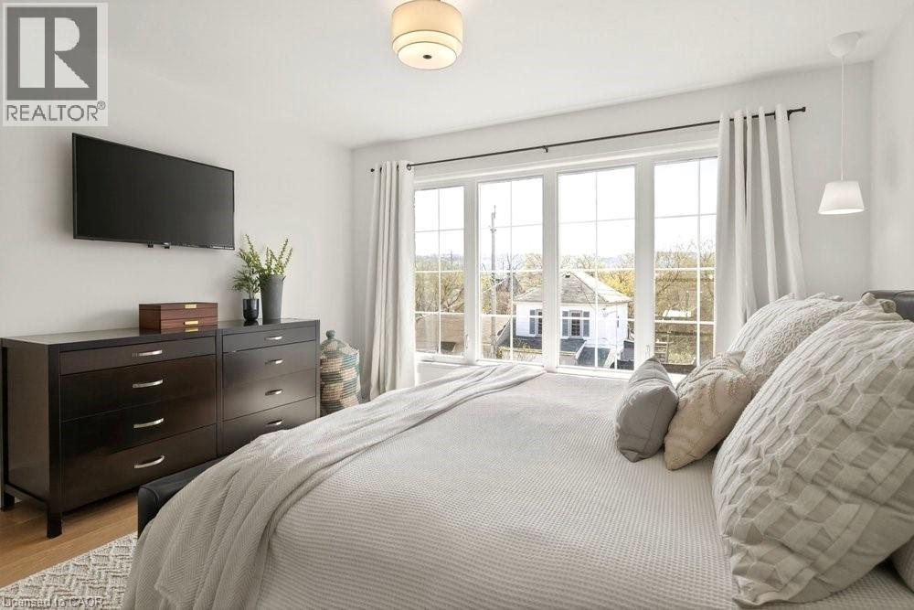 Expansive window wall with grid pattern, overhead flush mount light fixture, and wood-finish flooring - 128 Canada Street, Hamilton, ON - Indoor Photo Showing Bedroom