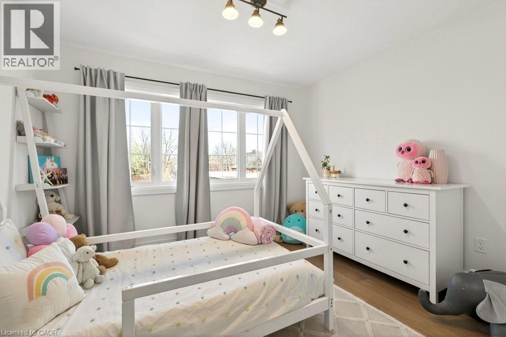 Bright room featuring multiple windows with natural light, wood-finish flooring, a white dresser with black hardware, and an overhead three-light fixture - 128 Canada Street, Hamilton, ON - Indoor Photo Showing Bedroom