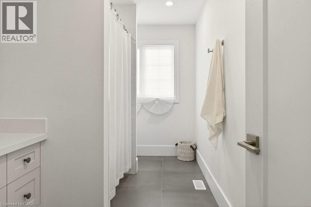 Bathroom featuring a white shower curtain, vanity with a white countertop and shaker-style cabinetry, a window with a white blind, and dark-toned floor tiles - 128 Canada Street, Hamilton, ON - Indoor Photo Showing Bathroom