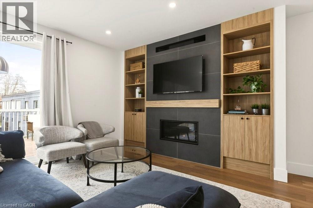 Living space featuring a tile-surround fireplace with a wood-finish mantel and integrated television mount - 128 Canada Street, Hamilton, ON - Indoor Photo Showing Living Room With Fireplace