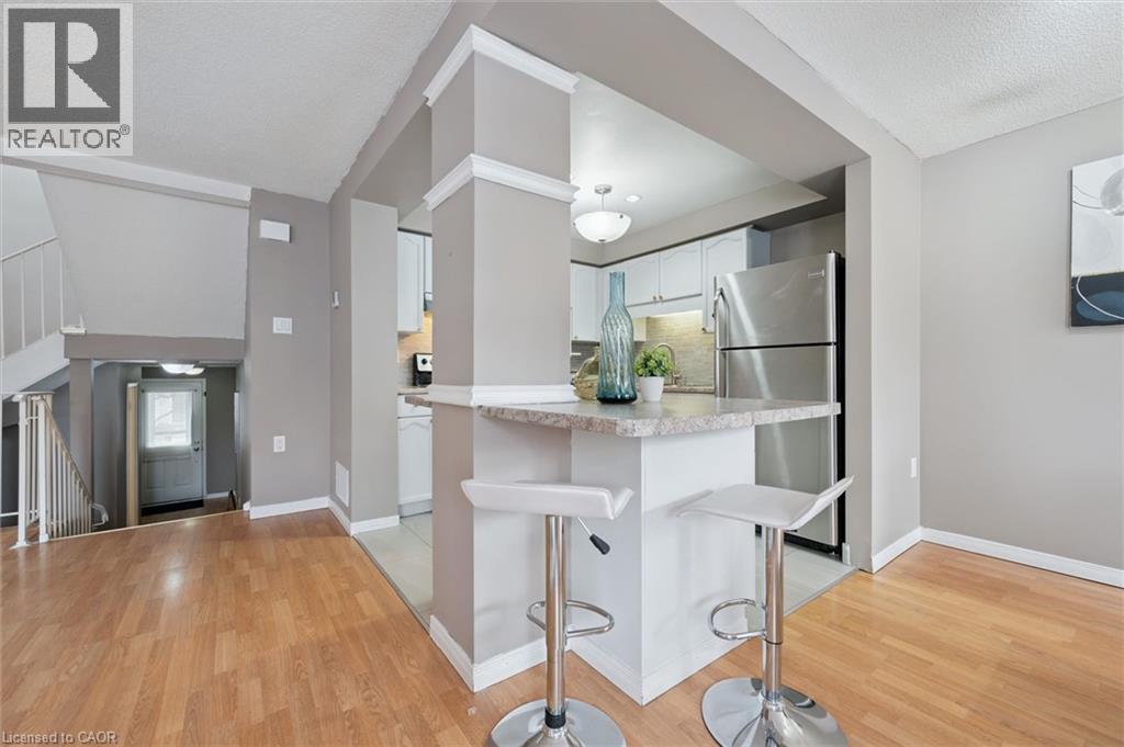 Kitchen breakfast bar with stone-finish countertop, light wood-finish flooring, white cabinetry, stainless steel refrigerator, and recessed lighting - 365 Pioneer Drive Unit# 25, Kitchener, ON - Indoor Photo Showing Other Room