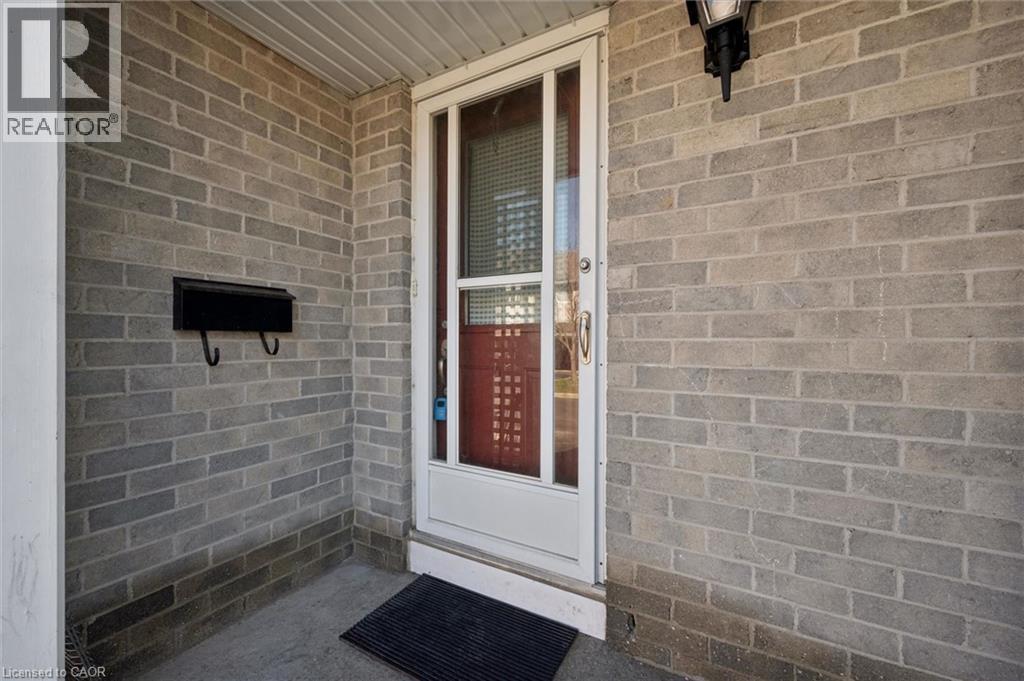 Entryway featuring light gray brick facade, a white storm door, and an exterior wall light fixture - 365 Pioneer Drive Unit# 25, Kitchener, ON - With Exterior