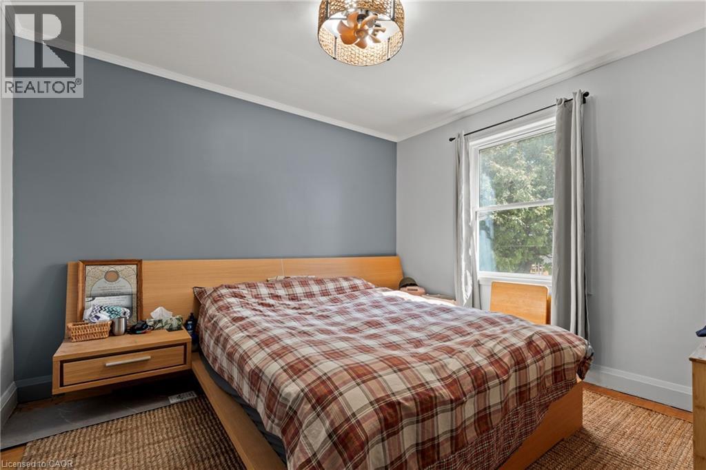 Bedroom featuring a single pane window with trim, crown molding, a built-in ceiling light fixture, wood-finish flooring, and a contrasting accent wall - 25 East 39Th Street, Hamilton, ON - Indoor Photo Showing Bedroom