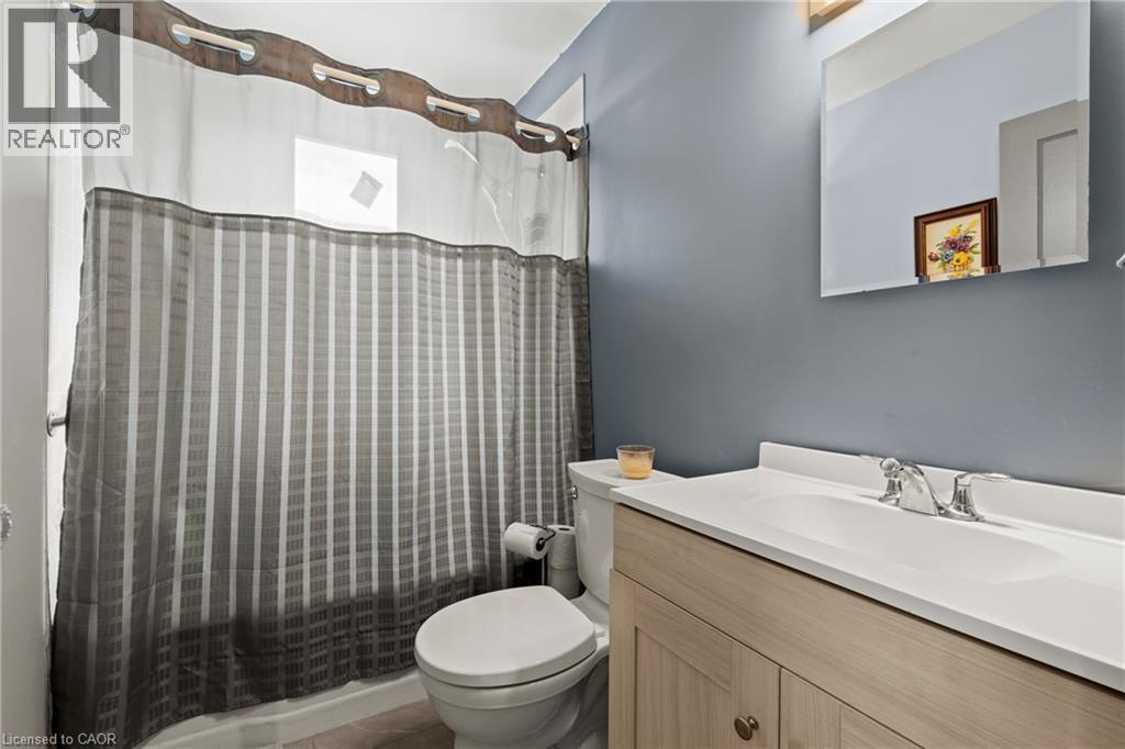 Bathroom featuring a tub/shower combination, light wood-finish vanity with an integrated sink, polished chrome faucet, and a wall-mounted mirror - 25 East 39Th Street, Hamilton, ON - Indoor Photo Showing Bathroom