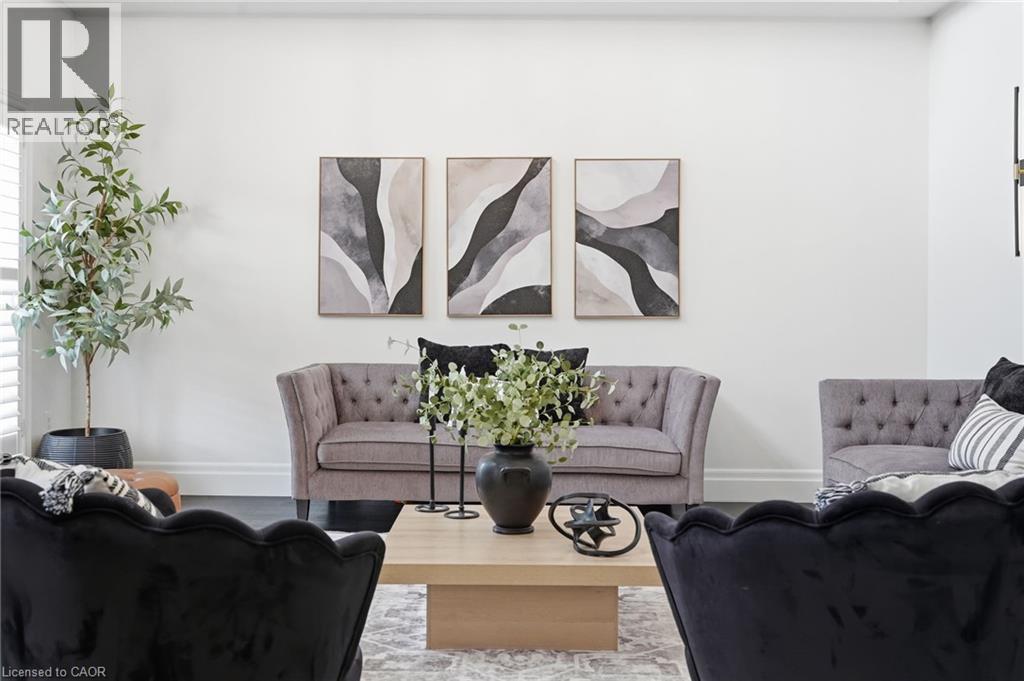 Light-filled living area featuring white walls, dark wood-finish flooring, and a large window with white plantation shutters - 47 Winners Way, Binbrook, ON - Indoor Photo Showing Living Room