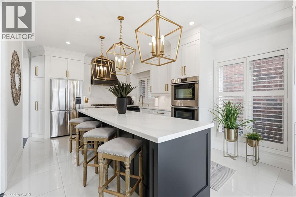 Modern kitchen featuring a large island with white countertop, white cabinetry with gold-tone hardware, stainless steel appliances, and white tile flooring - 47 Winners Way, Binbrook, ON - Indoor Photo Showing Other Room