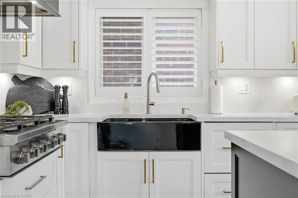 Kitchen featuring a black farmhouse-style sink, stainless steel gooseneck faucet, white shaker cabinetry with gold-toned hardware, white solid surface countertops, and a stainless steel professional-s - 47 Winners Way, Binbrook, ON - Indoor Photo Showing Kitchen