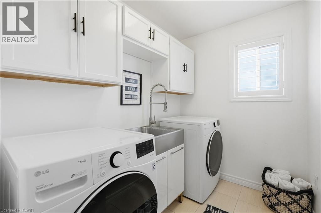 Dedicated laundry area featuring white shaker-style cabinetry with matte black hardware, a stainless steel utility sink with a gooseneck faucet, and a window with white plantation shutters - 47 Winners Way, Binbrook, ON - Indoor Photo Showing Laundry Room