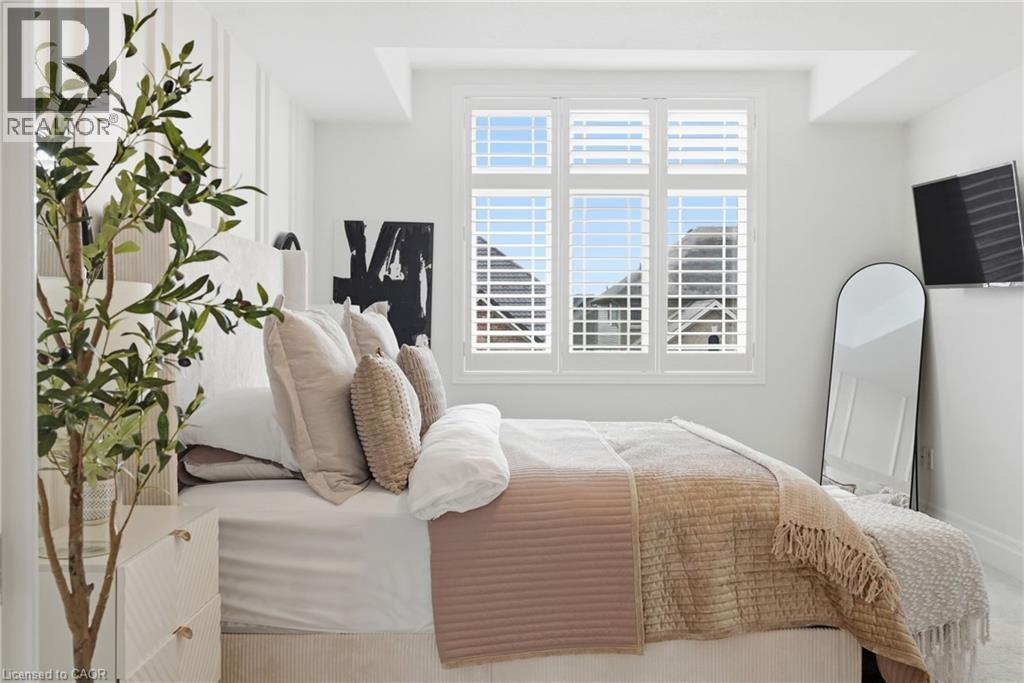 White interior with decorative wall paneling, a large window featuring white plantation shutters, and recessed ceiling lighting - 47 Winners Way, Binbrook, ON - Indoor Photo Showing Bedroom