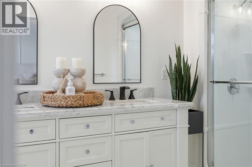Dual sink vanity with white cabinetry, stone countertop, matte black faucets, and arched mirrors - 47 Winners Way, Binbrook, ON - Indoor Photo Showing Bathroom