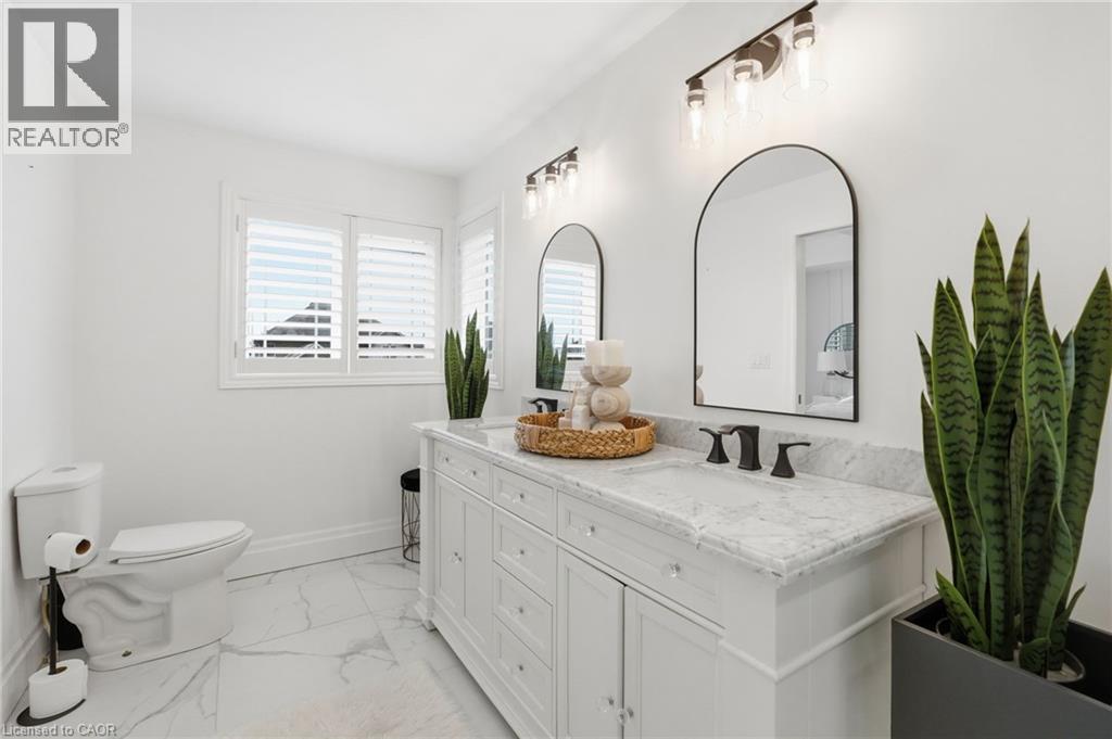 Bathroom featuring a white dual vanity with a marble-finish countertop, matte black fixtures, and two arched mirrors - 47 Winners Way, Binbrook, ON - Indoor Photo Showing Bathroom
