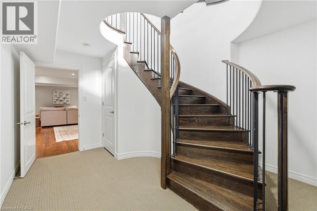 Curved hardwood staircase with wrought iron balusters and a dark wood handrail - 47 Winners Way, Binbrook, ON - Indoor Photo Showing Other Room