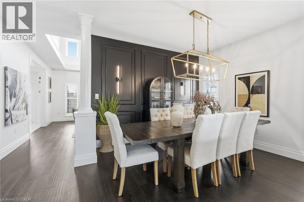 Formal dining area featuring dark wood-finish flooring, a decorative wall panel, and a gold-finish geometric chandelier - 47 Winners Way, Binbrook, ON - Indoor Photo Showing Dining Room
