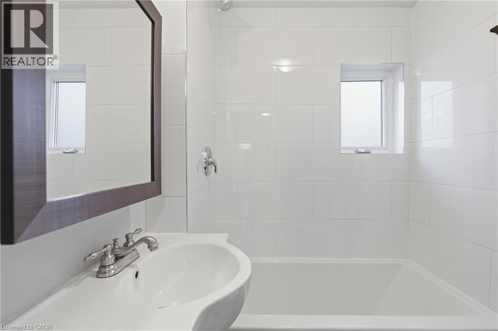 Bathroom featuring a vanity with a white basin and brushed nickel faucet, a framed mirror, a built-in bathtub, white subway tile surround, and an integrated window - 149 Lottridge Street, Hamilton, ON - Indoor Photo Showing Bathroom