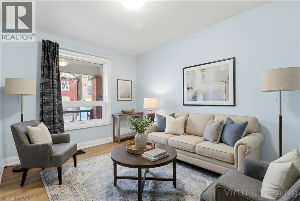 Living area featuring wood-finish flooring, light blue wall paint, a large window with white trim, a ceiling-mounted light fixture, and a decorative area rug - 149 Lottridge Street, Hamilton, ON - Indoor Photo Showing Living Room