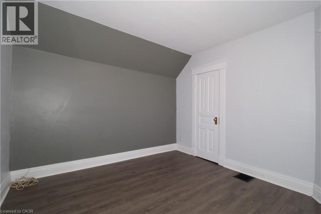 Room featuring wood-finish flooring, white baseboards, and a white panel door with brass hardware - 205 Duke Street E, Kitchener, ON - Indoor Photo Showing Other Room