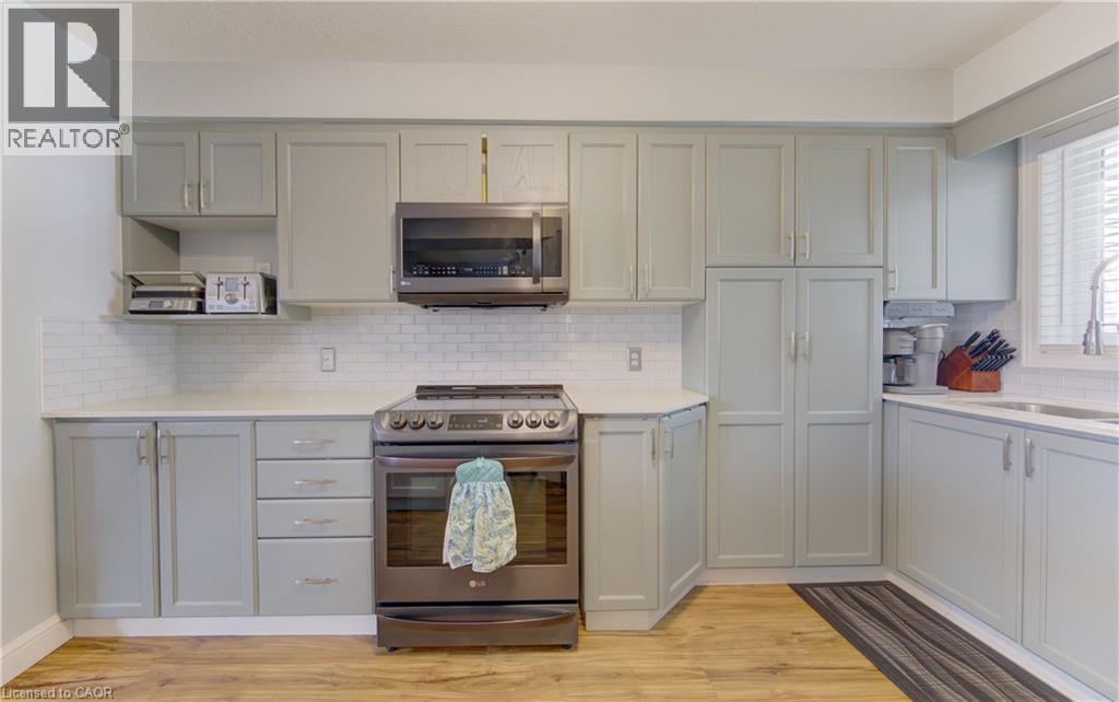 Kitchen featuring light gray cabinetry, stainless steel appliances, a white subway tile backsplash, light countertops, and wood-finish flooring - 512 Hidden Creek Drive, Kitchener, ON - Indoor Photo Showing Kitchen