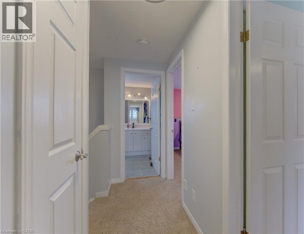 Carpeted hallway with white interior doors, leading to a bathroom featuring a white vanity with a mirror and multi-bulb light fixture - 512 Hidden Creek Drive, Kitchener, ON - Indoor Photo Showing Other Room