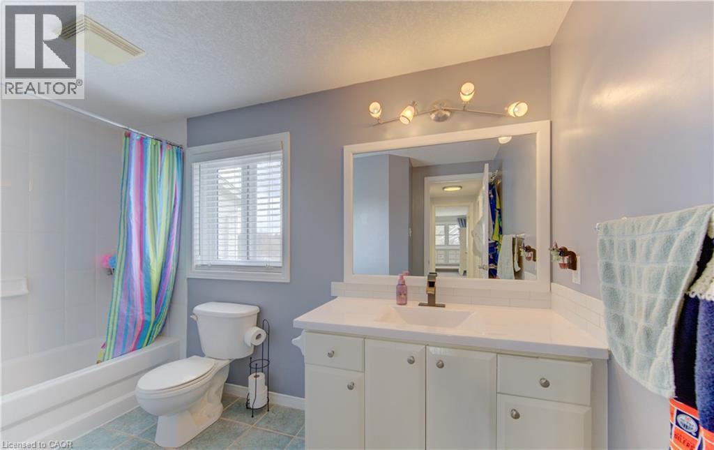 Bathroom featuring a white vanity with integrated sink, a large wall-mounted mirror, a modern vanity light fixture, and a window with blinds - 512 Hidden Creek Drive, Kitchener, ON - Indoor Photo Showing Bathroom