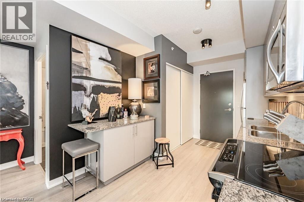 Modern kitchen featuring stainless steel appliances, granite countertops, and light wood-finish flooring - 85 Duke Street W Unit# 507, Kitchener, ON - Indoor
