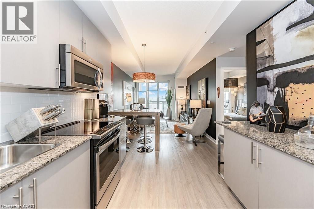 Modern kitchen featuring light gray cabinetry, stainless steel appliances, speckled stone countertops, and a subway tile backsplash - 85 Duke Street W Unit# 507, Kitchener, ON - Indoor Photo Showing Kitchen With Upgraded Kitchen
