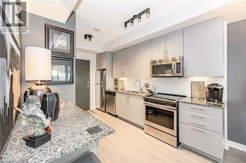 Modern kitchen featuring light gray cabinetry, stainless steel appliances, granite countertops, and light wood-finish flooring - 85 Duke Street W Unit# 507, Kitchener, ON - Indoor Photo Showing Kitchen With Double Sink With Upgraded Kitchen