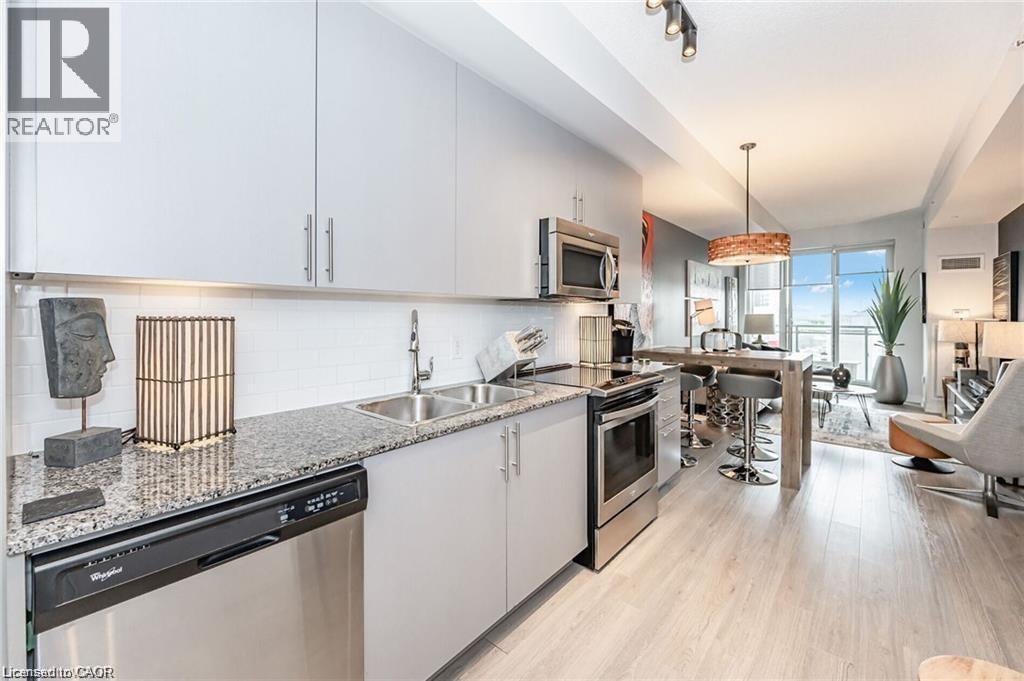 Kitchen featuring light grey cabinetry, granite countertops, and stainless steel appliances including a built-in microwave, range, and dishwasher - 85 Duke Street W Unit# 507, Kitchener, ON - Indoor Photo Showing Kitchen With Double Sink