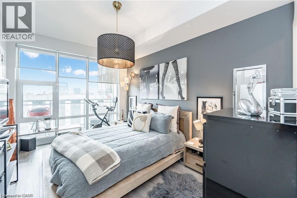 Floor-to-ceiling windows with roller shades, wood-finish flooring, a contemporary drum pendant light, and a neutral color palette - 85 Duke Street W Unit# 507, Kitchener, ON - Indoor Photo Showing Bedroom