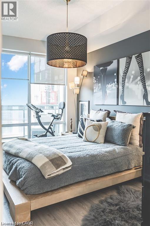 Bedroom featuring a drum pendant light fixture, floor-to-ceiling windows with roller shades, and light-toned wood-finish flooring - 85 Duke Street W Unit# 507, Kitchener, ON - Indoor Photo Showing Bedroom