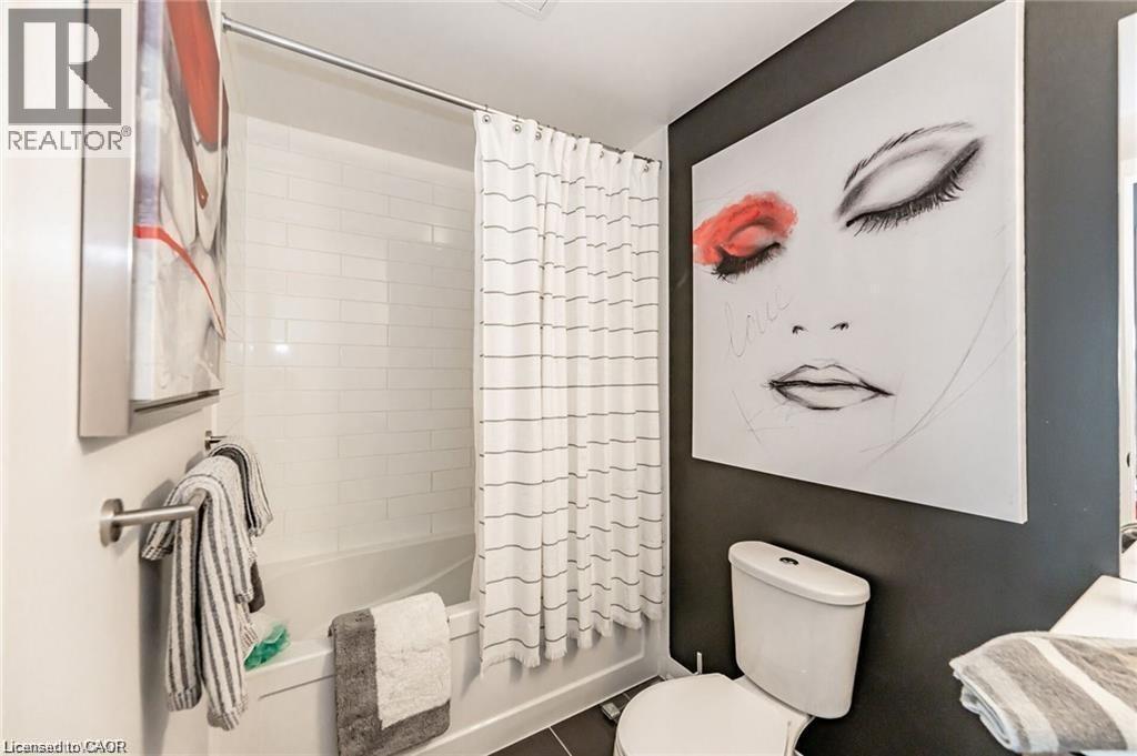 Bathroom featuring a tub/shower combination with white subway tile surround, white toilet, and dark-colored wall accent - 85 Duke Street W Unit# 507, Kitchener, ON - Indoor Photo Showing Bathroom