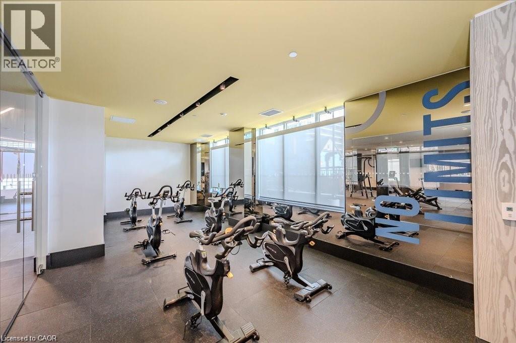 Dedicated spin studio featuring multiple stationary bikes, expansive mirrored wall, floor-to-ceiling windows with roller shades, and durable rubber flooring - 85 Duke Street W Unit# 507, Kitchener, ON - Indoor Photo Showing Gym Room